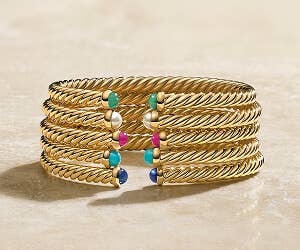 Stack of gold David Yurman cable bracelets with a variety of stones.