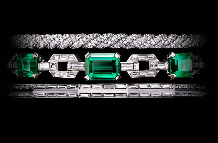 A colour photo shows a close-up of the central portion of a David Yurman High Jewelry Stax three-row bracelet displayed against a black background. The jewellery is crafted from 18K white gold and is fully set with three large, emerald-cut Colombian emeralds and brilliant-, baguette- and custom-cut white diamonds.