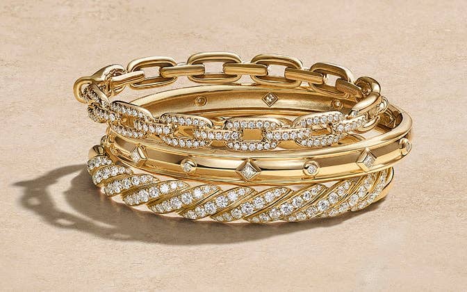 A mixed stack of gold David Yurman bracelets with and without diamonds.