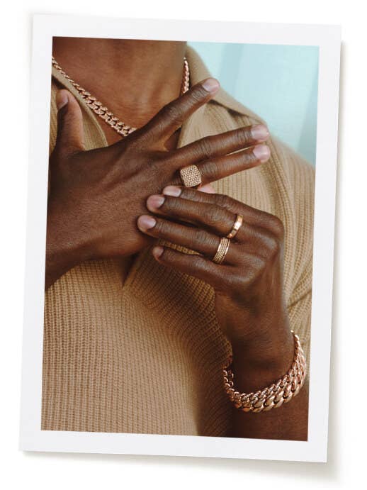 An image of Aldis Hodge wearing a gold band and gold curb chain necklace.