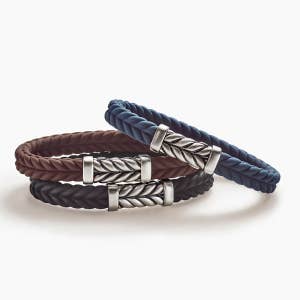 Three David Yurman rubber bracelets in blue, brown and black with silver cable closure.