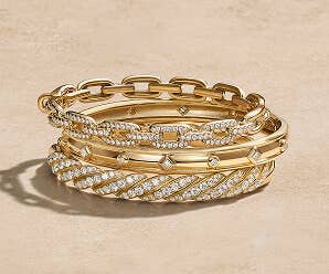 A mixed stack of gold David Yurman bracelets with and without diamonds.