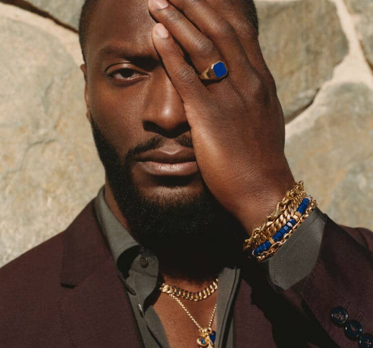 An image of Aldis Hodge wearing bracelets, amulets and signet ring.