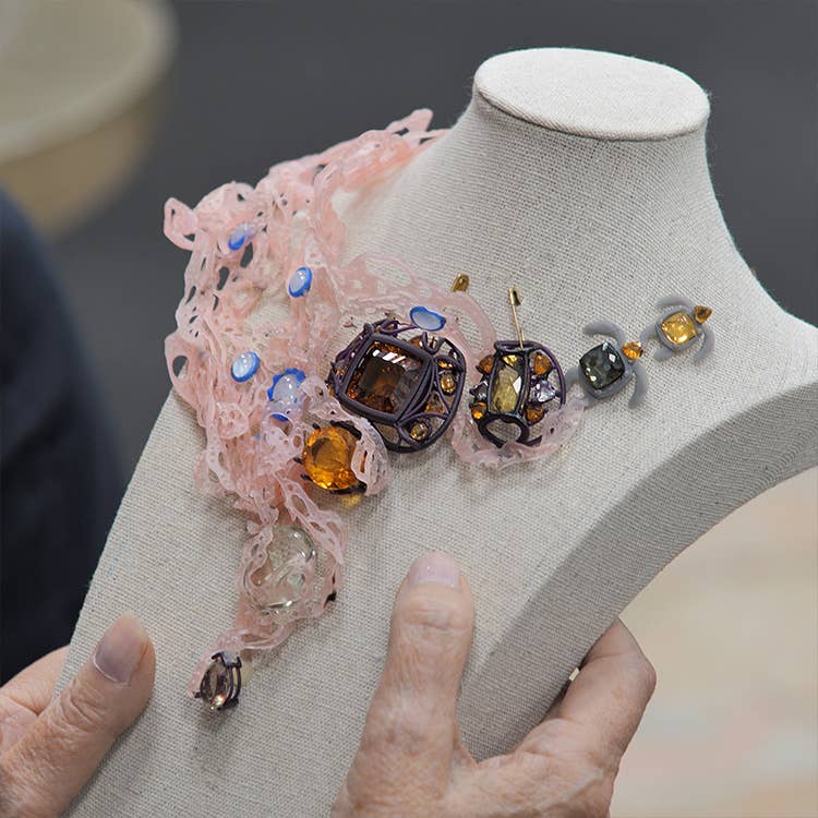 An image of gems on a mannequin layed out into a necklace.