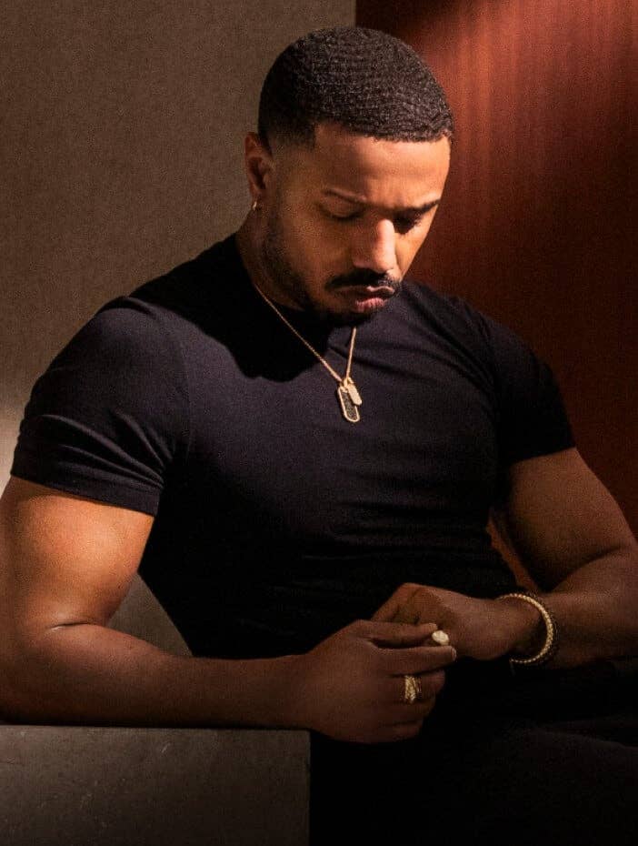 Michael B. Jordan wearing a gold David Yurman necklace with a tag and pendant.