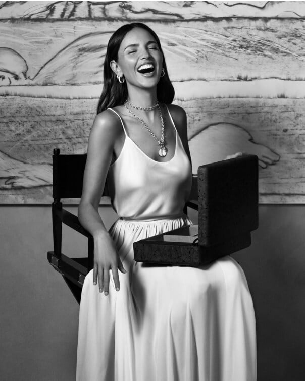 Eiza González sitting on a chair laughing.