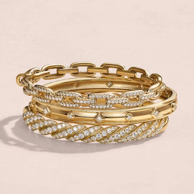 A stack of gold David Yurman women's bangle bracelets with and without diamonds.